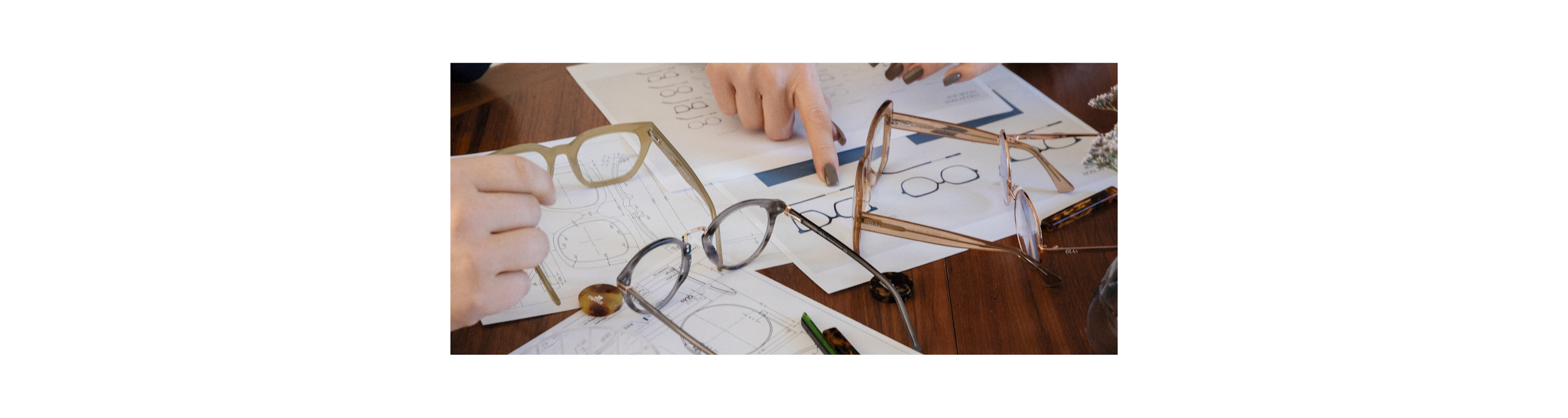 Reading glasses lying on a table surrounded by technical drawings and acetate samples
