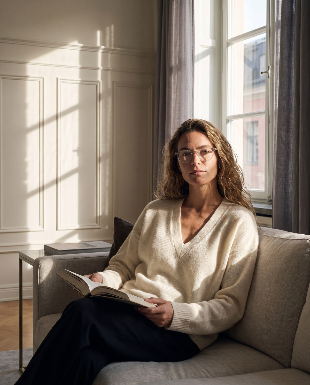 Een vrouw leest op de bank in laag septemberlicht, met de leesbril Emily Quartz.